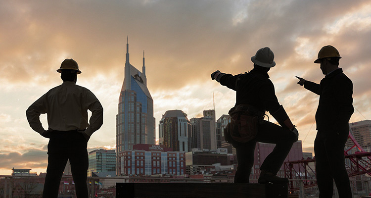 skyline of Nashville, Tennessee, at sunset, with three individuals in hard hats looking out over the cityscape