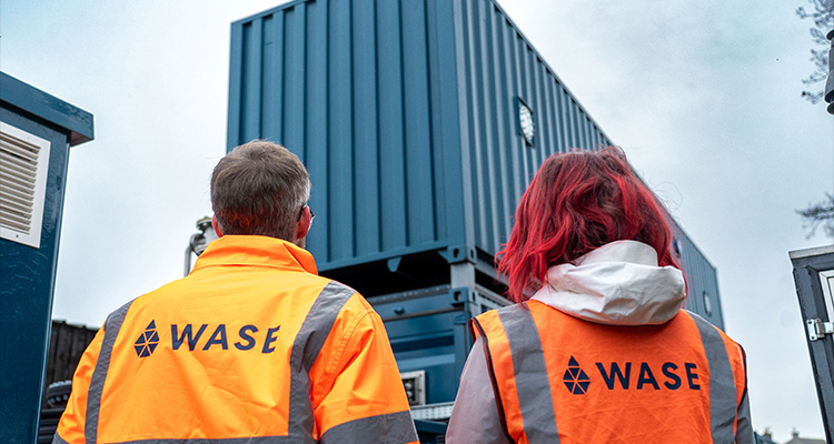 two individuals wearing high-visibility vests with the logo and name "WASE" on the back