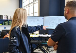 two people, discussing technical drawings on computer screens.