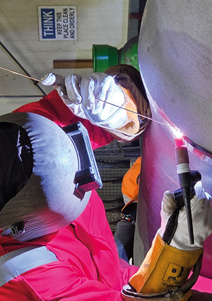  a welder in red overalls and protective gear is shown working on a project
