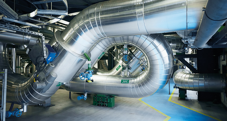 an industrial plant interior with large, silver-insulated metal pipes arranged in complex loops and curves
