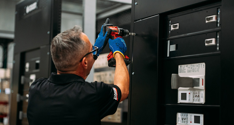 a technician using a power drill to assemble or service an industrial electrical switchgear or control panel cabinet
