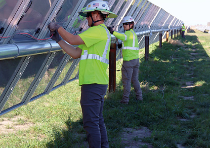 workers installing wiring and components on a ground-mounted solar panel array