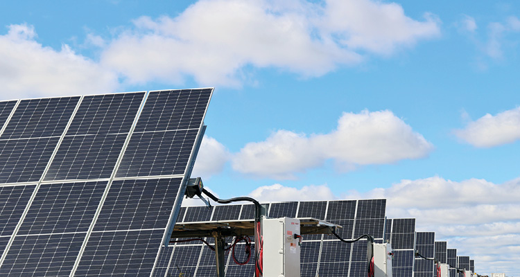 a large-scale ground-mounted photovoltaic solar farm with rows of solar panels under a partly cloudy sky