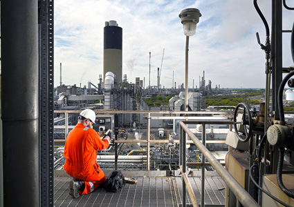 worker in an orange jumpsuit and hard hat conducting maintenance or monitoring on a high-altitude platform at the VPI Immingham combined heat and power station
